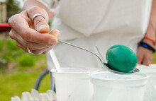 The Hand Holds A Spoon And Pulls Out A Green Egg From Easter Paints