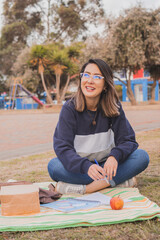 Wall Mural - Female Hispanic college student sitting on the grass and studying in the park