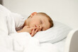 © Aleksandr - The child sleeps sweetly with his fingers to his mouth on a white crib. A little boy has sweet dreams
