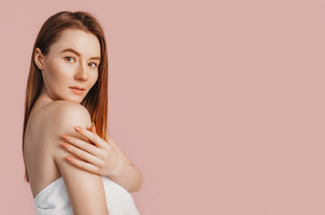 Beautiful sensual young girl with clean skin on a pink background with a mockup. Topless woman in a towel. The concept of spa treatments, natural beauty and care, youth, cream and mask, freshness