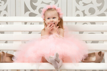 two-year-old child. a beautiful little girl in a smart pink dress sits on a wooden bench and laughs.