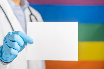 Doctor hand holding a white paper while standing with the rainbow (LGBT) flag background. Space for text. Medical and information concept