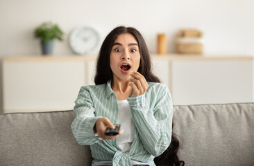 Poster - Shocked Indian woman sitting on couch, eating popcorn and watching exciting TV show or movie at home