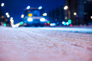 Winter night in the big city, the headlights of the arriving van. Close up view of snow on the asphalt level