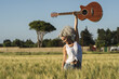 Curly-haired Spanish cute woman posing in a wheat field with an acoustic guitar