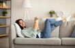 © Prostock-studio - Stay home activities. Young Indian woman lying on couch with open book indoors, relaxing on Sunday morning