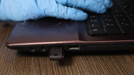 Spy hacker in blue gloves theft downloading files from notebook to USB flash.