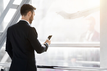 Back view of middle-aged entrepreneur going for departure, checking phone