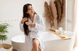 © Prostock-studio - Brunette Female Brushing Hair With Hairbrush Sitting On Bathtub Indoor