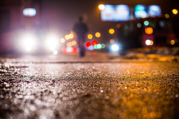 Wall Mural - Rainy night in the big city, glare from the headlights of the car parked and people passing near. Close up view from the sidewalk level