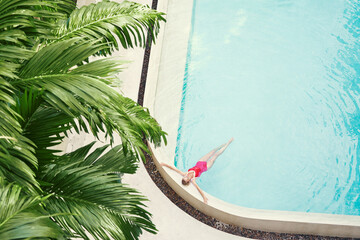 Poster - Enjoying suntan. Vacation concept. Top view of slim young woman in red swimsuit in the tropical swimming pool.