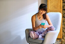 Smiling Woman Using Mobile Phone While Sitting On Arm Chair At Home