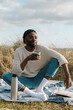 © Boy/Westend61 - Smiling relaxed man sitting on blanket amidst dried plants while drinking tea against cloudy sky