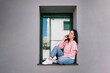 © Lupe Rodriguez/Westend61 - Smiling woman talking on smart phone while sitting on window sill