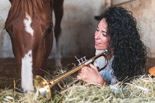 Woman With Trumpet Day Dreaming While Lying On Hay By Horse In Stable