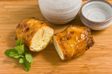 Wall Mural - top view, close up of a freshly fried breakfast spring roll, cut in half to see cooked eggs and sake ceramic container and cup with sprig of mint on wood cutting board