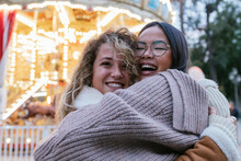 Laughing Female Friends Embracing Against Illuminated Carousel