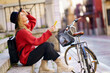 © Javier S√°nchez Mingorance/Westend61 - Woman with mobile phone looking up while sitting by bicycle on steps