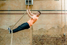 Male Man Hanging On Rope By Brick Wall At Gym