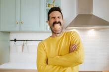 Man With Tangerine Fruit In Mouth And Arms Crossed At Kitchen