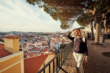Wall Mural - Traveling by Portugal. Young traveling woman enjoying old town Lisbon view, red tiled roofs and ancient architecture.