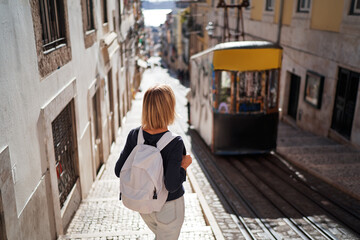 Wall Mural - Traveling by Portugal. Happy young woman with rucksack walking by streets in Lisbon.