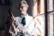 © Robijn Page/Westend61 - Smiling businesswoman looking at mobile phone while standing at window in home office