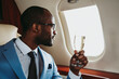 © OneInchPunch/Westend61 - Young businessman with champagne looking through window in private jet