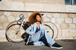 © Rafa Cort√©s/Westend61 - Woman with bicycle sitting on footpath against building during sunny day