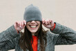 © Xavier Lorenzo/Westend61 - Smiling woman covering eyes through knit hat against wall