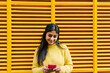 © Xavier Lorenzo/Westend61 - Woman with mobile phone standing at yellow wall