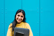 © Xavier Lorenzo/Westend61 - Happy woman with digital tablet and laptop bag against blue wall