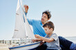 © Roger Richter/Westend61 - Father and son preparing toy sailboat together while sitting on pier