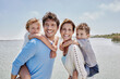 © Roger Richter/Westend61 - Smiling parents piggybacking children by lake on sunny day