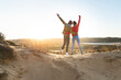© steve brookland/Westend61 - Young couple standing with hand raised and arm around on each other against sky
