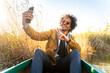 © steve brookland/Westend61 - Young man gesturing peace sign while taking selfie through mobile phone sitting in canoe on river