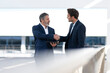 © steve brookland/Westend61 - Mature entrepreneur holding digital tablet while doing handshake with colleague standing at office building terrace