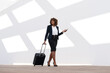 © steve brookland/Westend61 - Businesswoman with mobile phone and wheeled luggage walking against white wall
