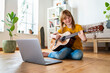 © steve brookland/Westend61 - Smiling redhead girl playing guitar while e-learning through laptop at home
