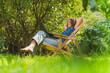 © steve brookland/Westend61 - Smiling mid adult woman with hands behind back looking at laptop while sitting on chair in garden