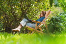 Smiling Mid Adult Woman With Hands Behind Back Looking At Laptop While Sitting On Chair In Garden