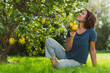 © steve brookland/Westend61 - Smiling woman holding lemons while looking at tree on grass