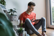 © Uwe Umst√§tter/Westend61 - Smiling young man using digital tablet while sitting against wall at home