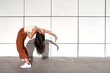 © Veam/Westend61 - Young woman bending backwards with hand on hip against wall during sunny day