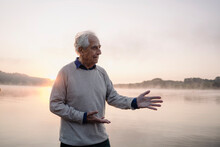 Senior Man Gesturing While Standing Against Lake During Sunrise