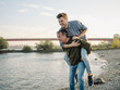 © Gustafsson/Westend61 - Happy father giving piggyback ride to son at riverbank