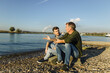 © Gustafsson/Westend61 - Father giving advice to son while sitting on rock at riverbank during sunny day