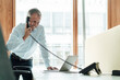 © Gustafsson/Westend61 - Smiling male entrepreneur using laptop while talking on telephone at desk