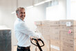 © Gustafsson/Westend61 - Smiling senior businessman holding pallet jack in warehouse