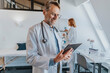 © Mareen Fischinger/Westend61 - General practitioner using digital tablet while standing with coworker in background at clinic